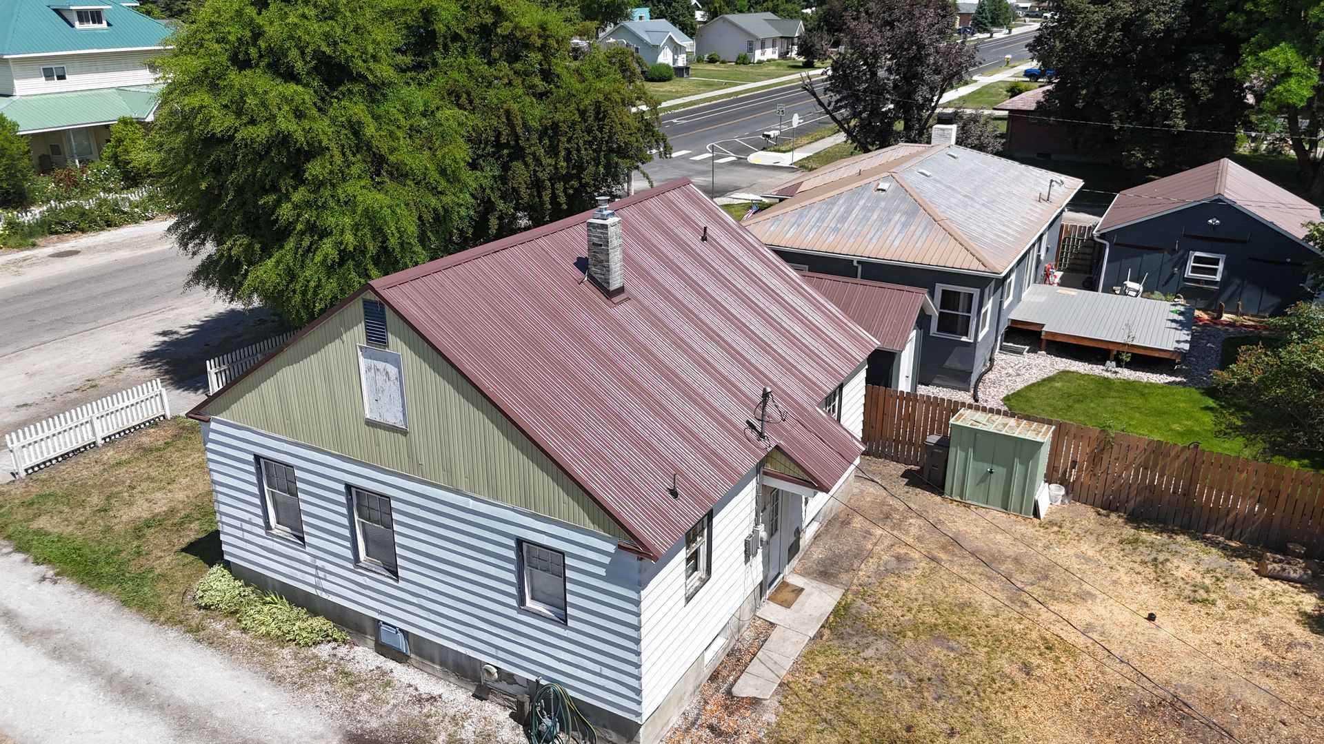 Aerial view of a white house with a red roof and backyard, surrounded by trees and neighboring homes