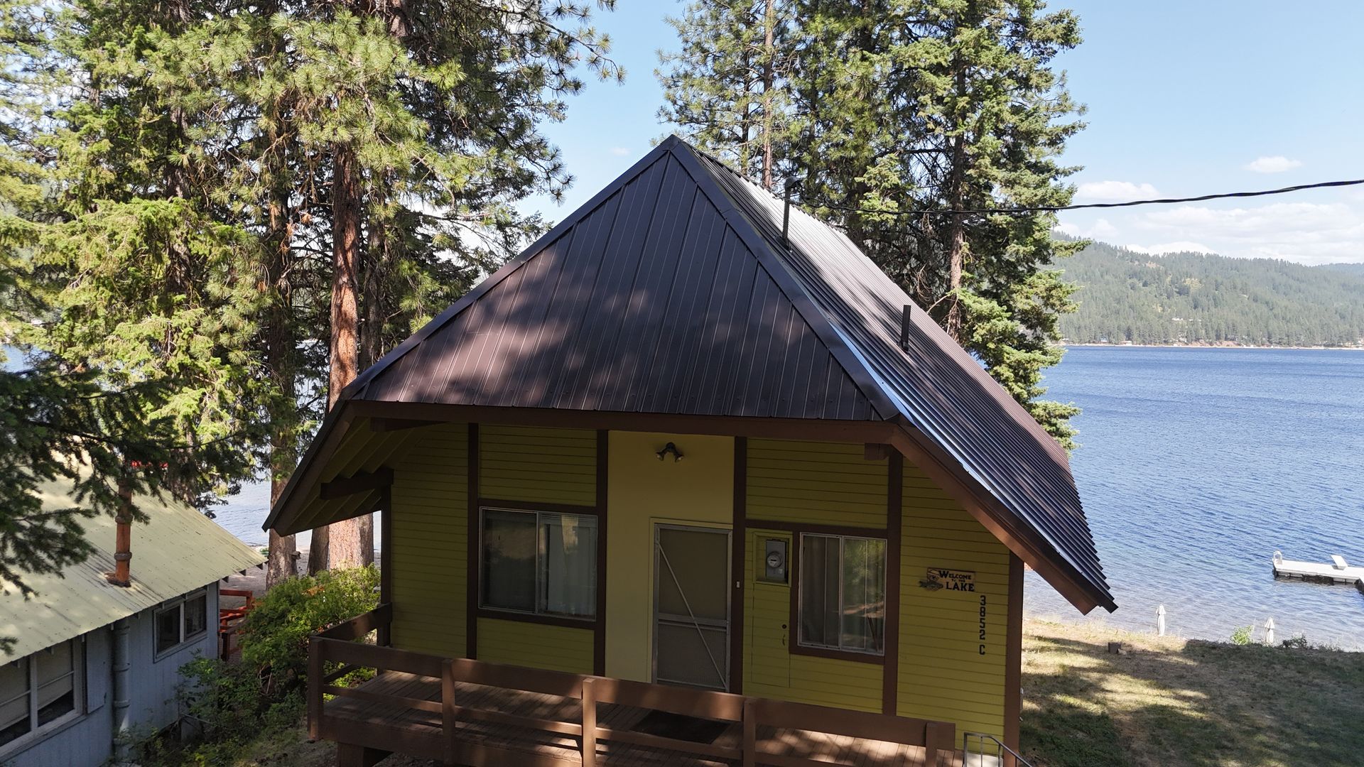 Yellow lakeside cabin with a dark roof, surrounded by trees and overlooking water