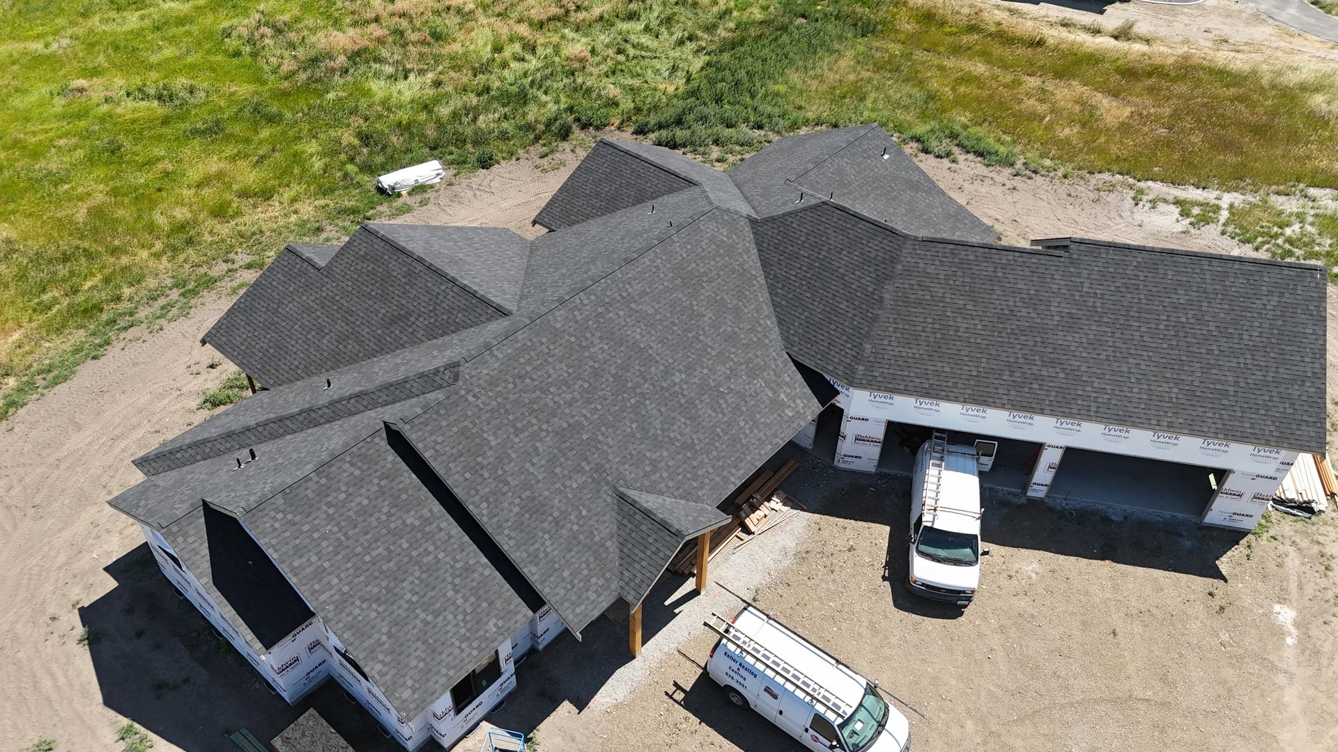 Aerial view of a large gray-roofed house with two white vehicles in the driveway.