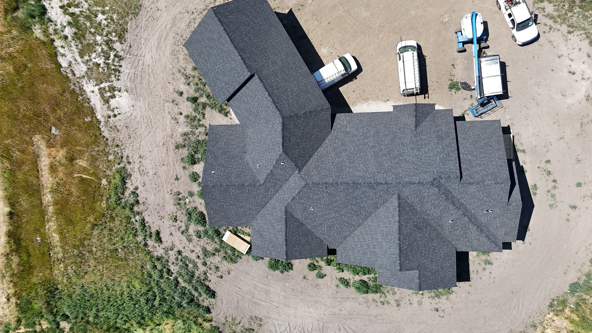 Aerial view of a dark gray-roofed building with several white vehicles parked on a gravel lot.