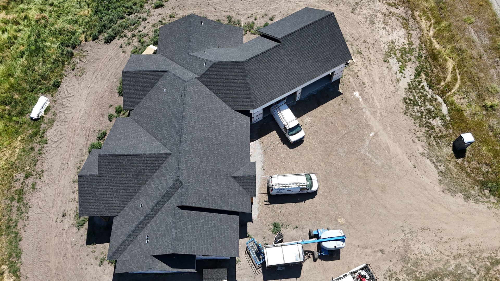Aerial view of a large dark-roofed house with vehicles parked on a gravel lot.