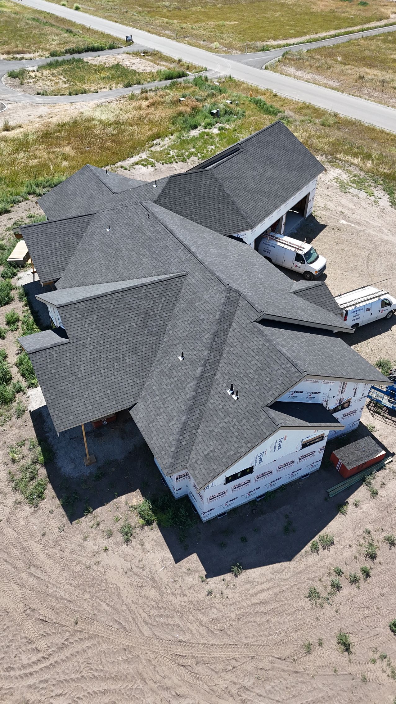 Aerial view of a large house with a dark gray roof in a sandy, unfinished neighborhood.