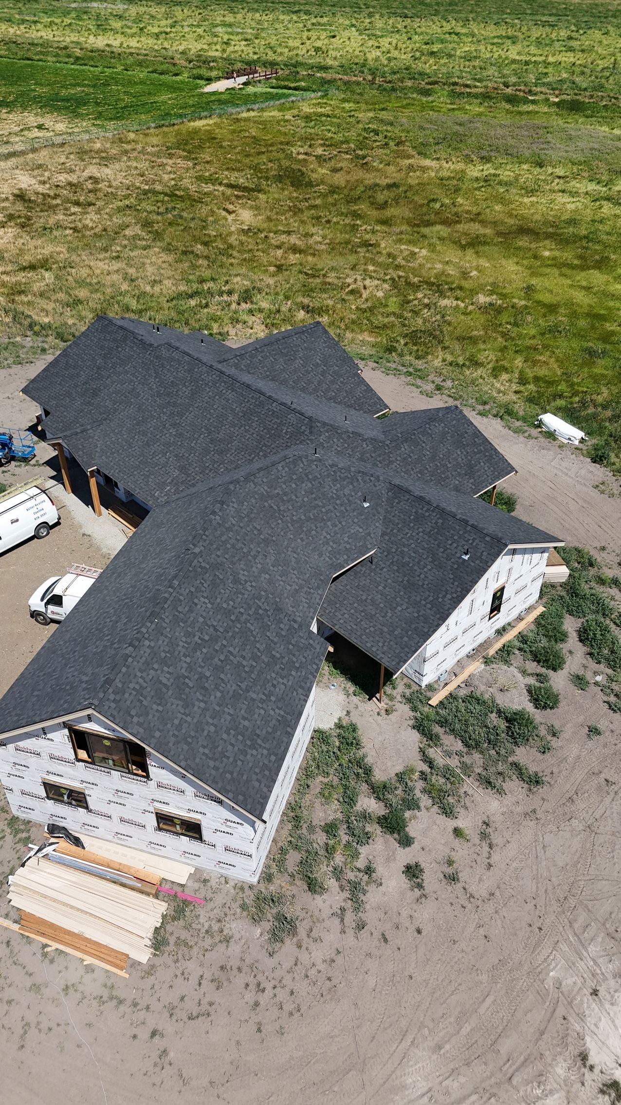 Aerial view of a gray-roofed house under construction beside a grassy field