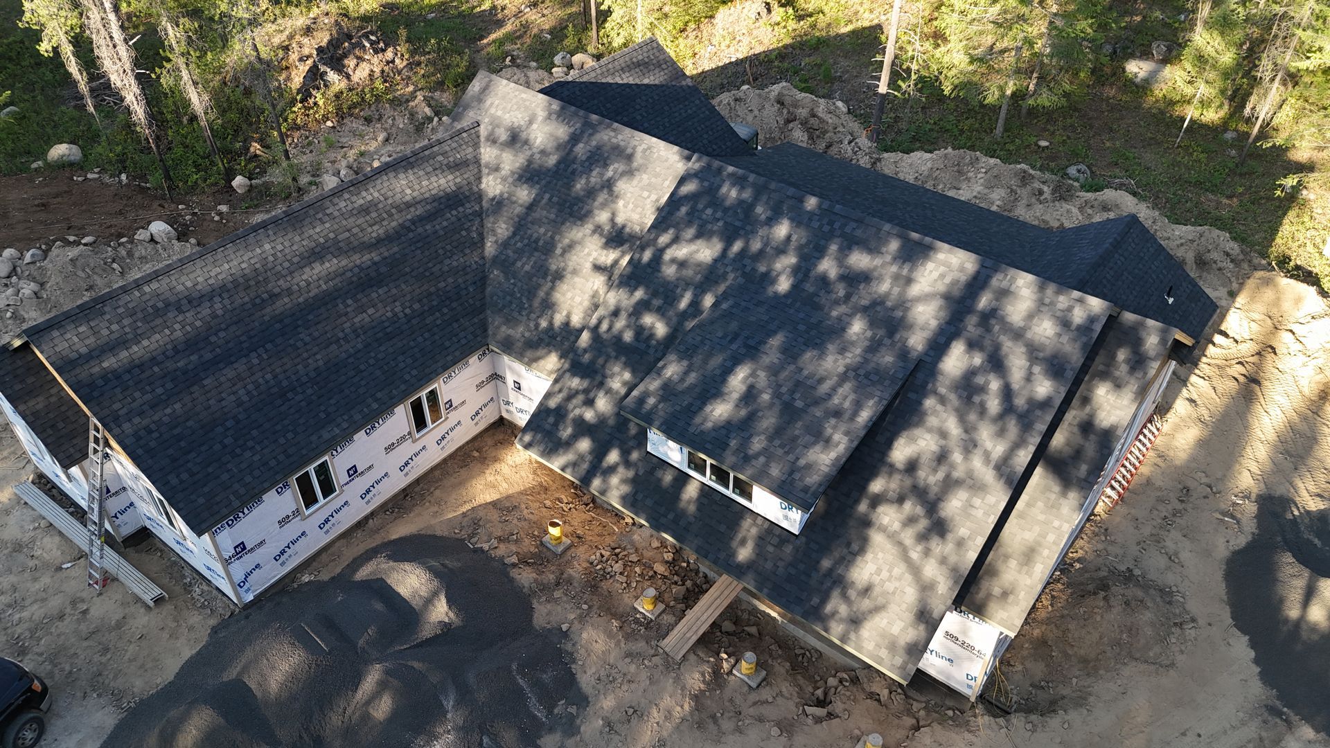 Aerial view of a white house with a dark roof, surrounded by trees and a driveway.