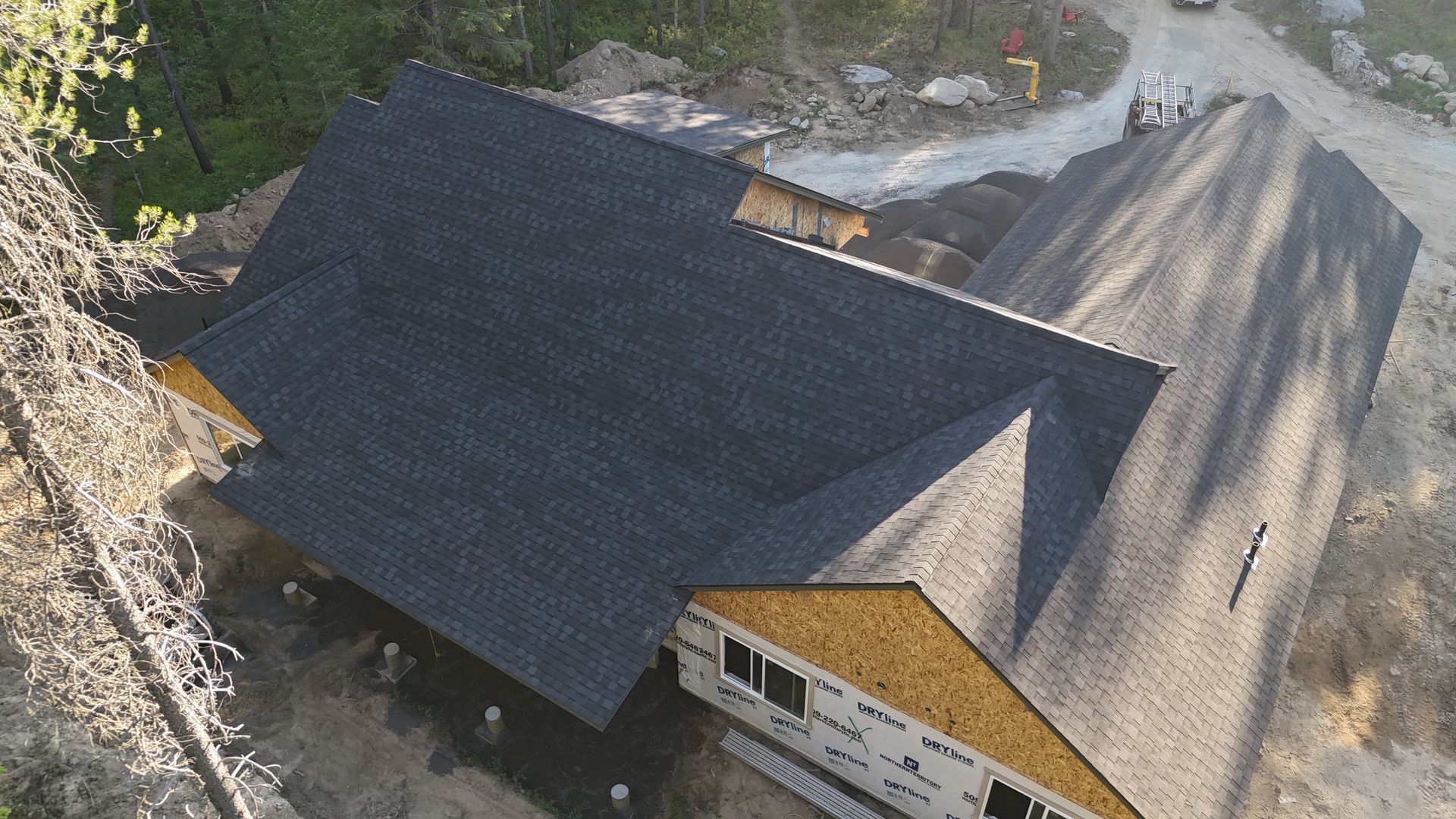Aerial view of a large house with a dark roof beside a rocky hillside and gravel road.