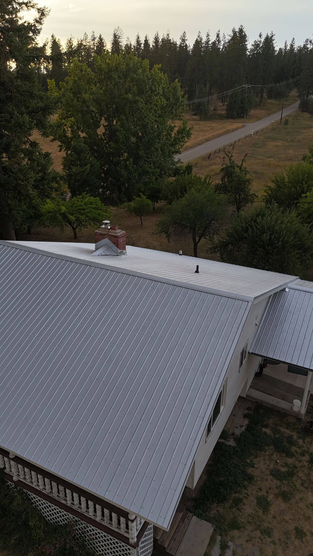 Rural house with a white roof beside trees and a dirt road at sunset