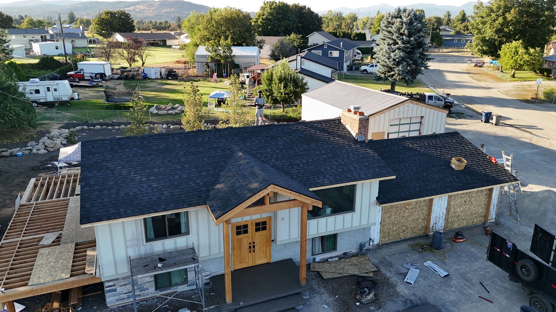 Newly roofed house with white siding and a wooden front entry, seen from above in a suburban neighborhood.