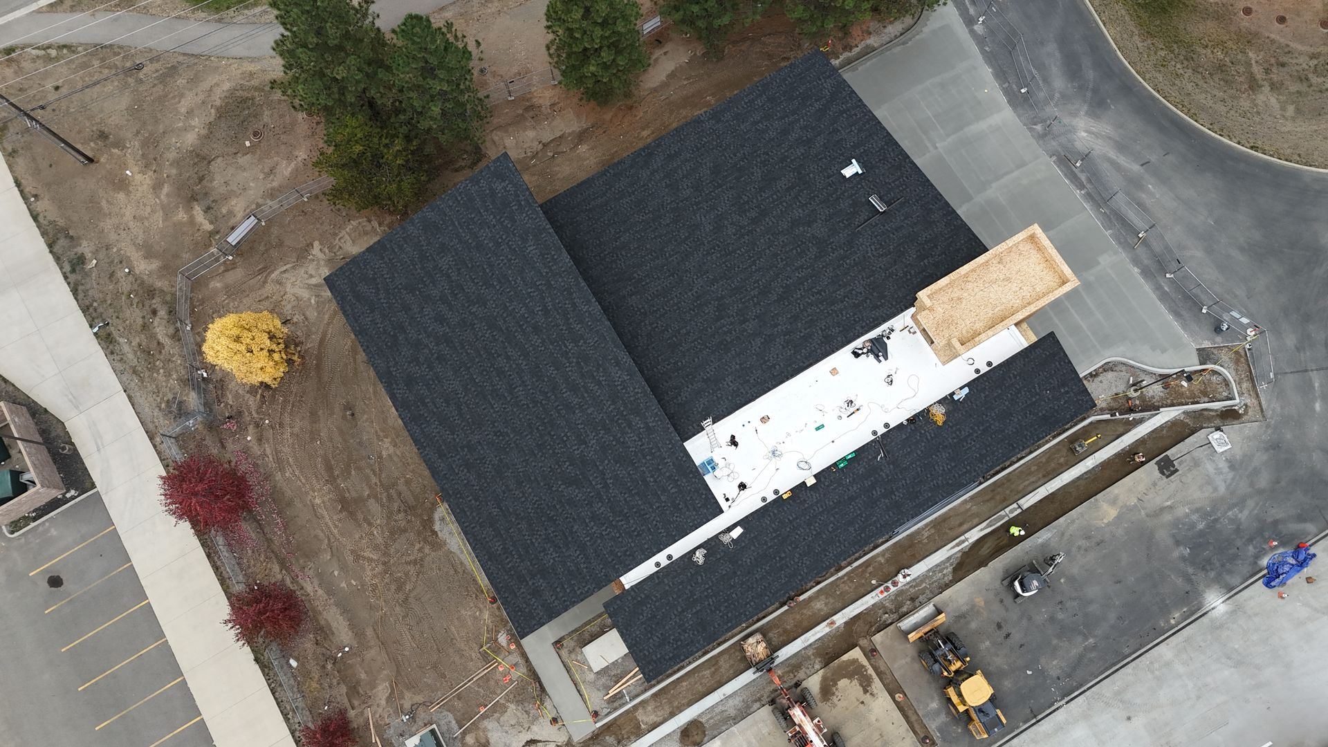 Aerial view of a house with dark roof, white roof section, and surrounding driveway and yard.