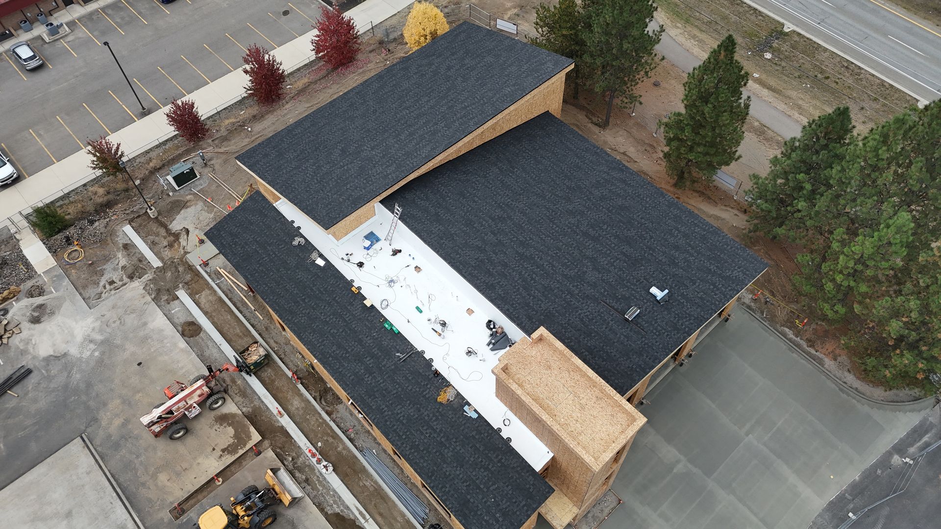 Aerial view of a building under construction with dark roofing and exposed white underlayment.