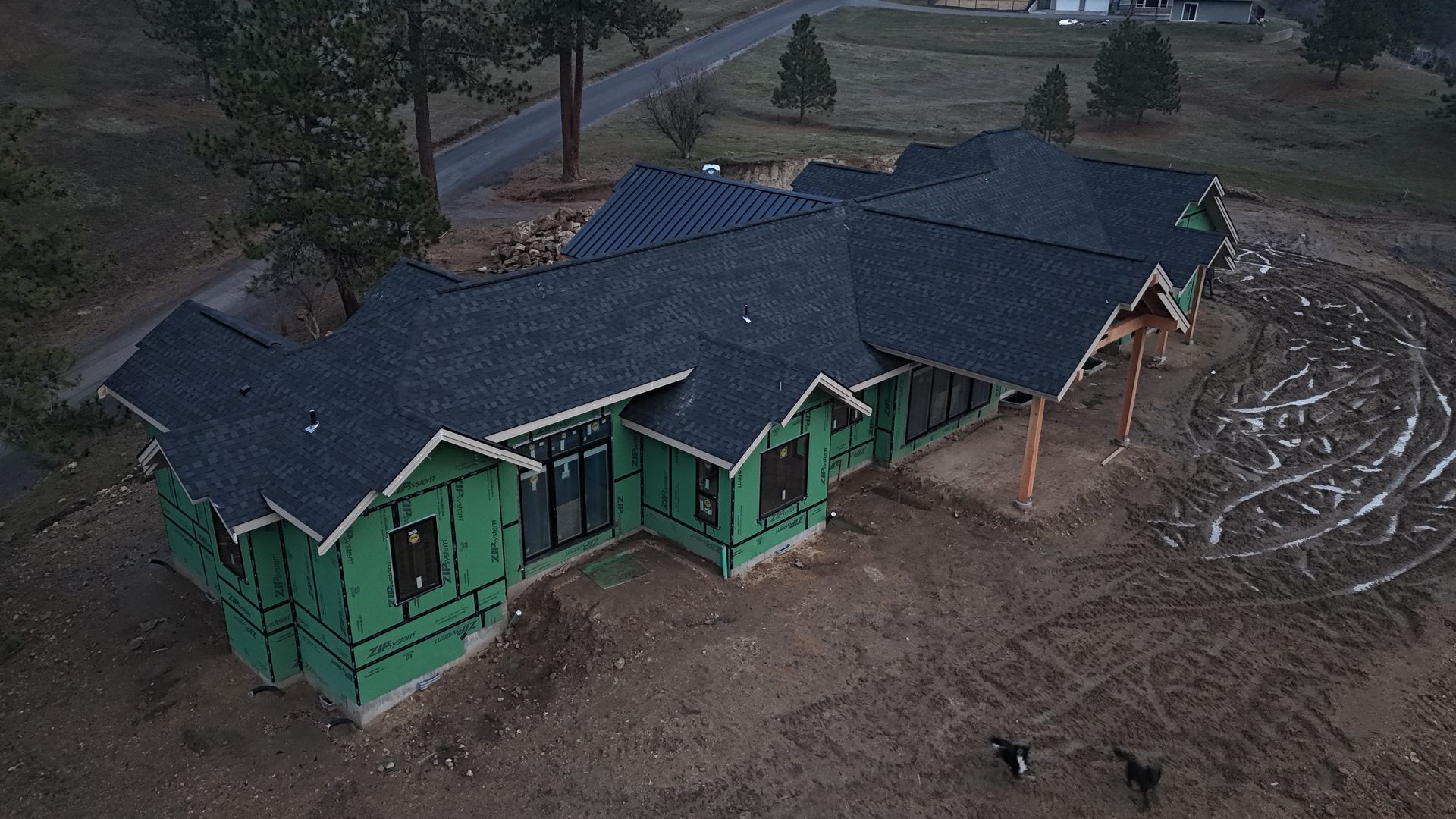Green house with dark roof surrounded by muddy floodwater and debris at dusk