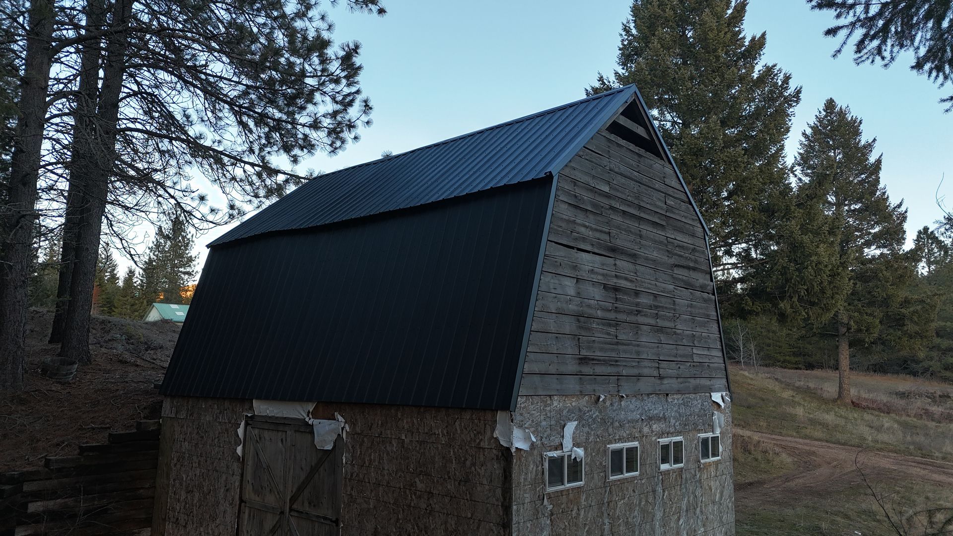 Rustic barn with black metal roof and stone lower walls in a wooded rural setting
