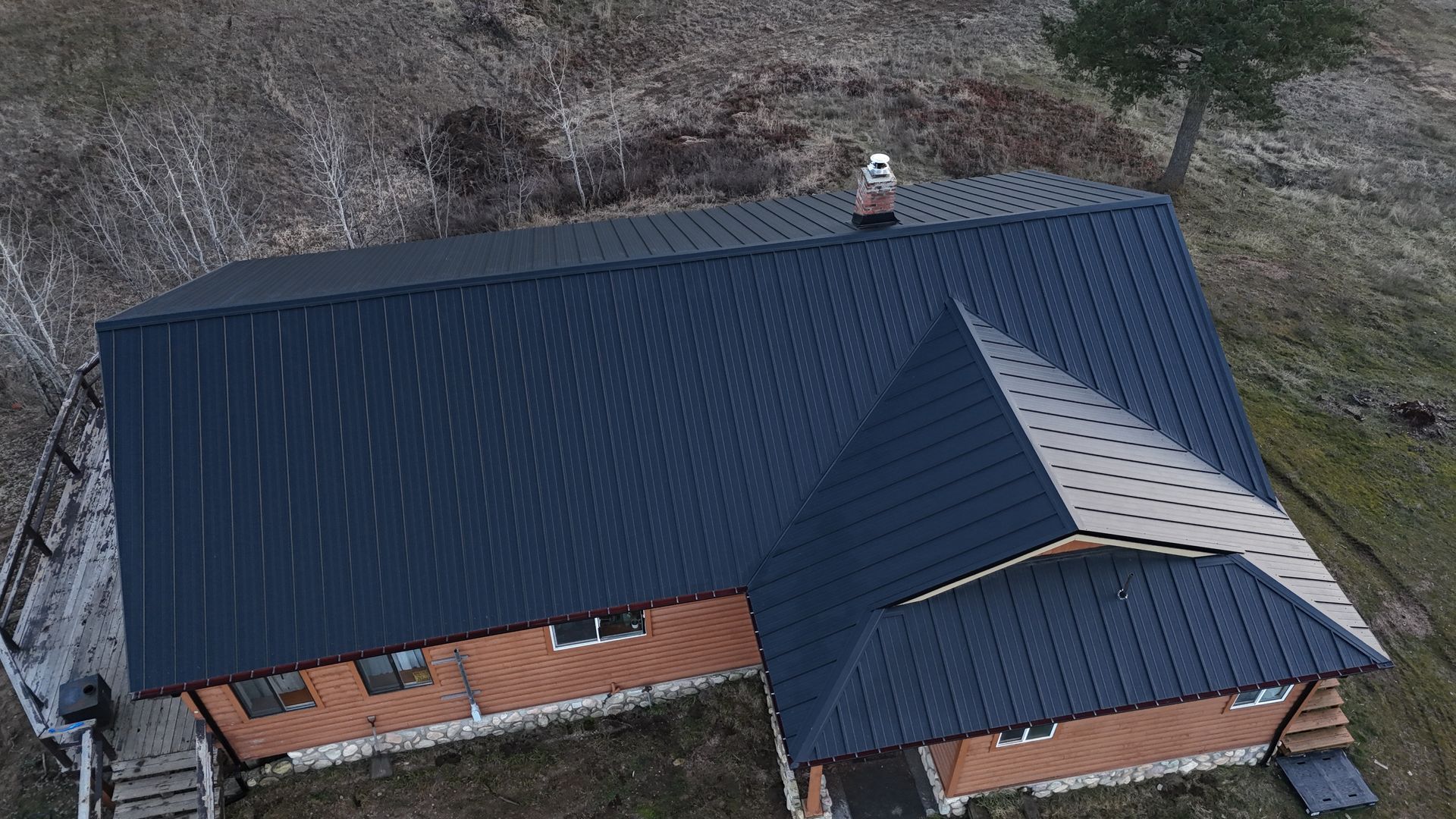 Aerial view of a house with a dark metal roof and brick walls in a grassy yard