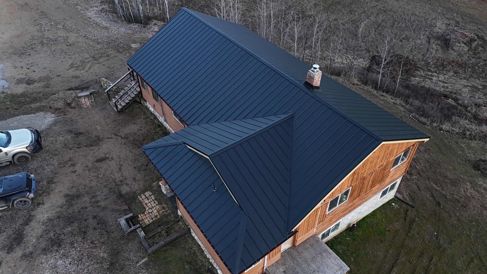 Aerial view of a brick house with a dark blue roof and chimney, beside a gravel yard.