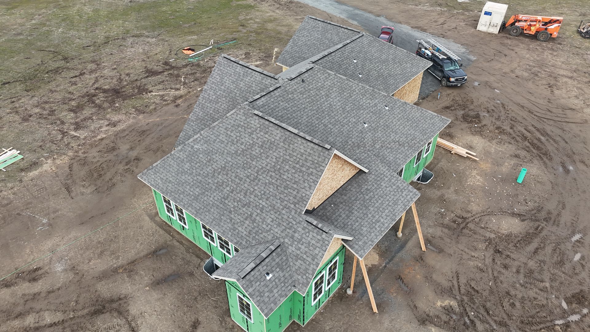 Aerial view of a house under construction with a gray roof and green walls on a dirt lot.