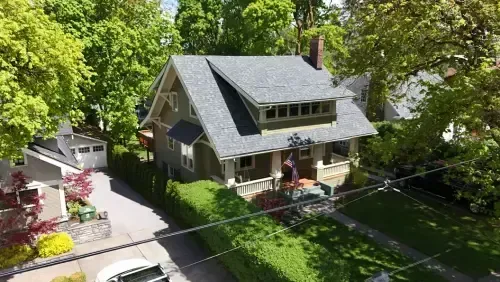 Aerial view of a gray house with a green lawn, surrounded by trees and a driveway.