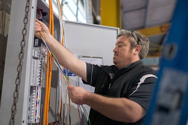 An electrician is working on an electrical box in a factory.