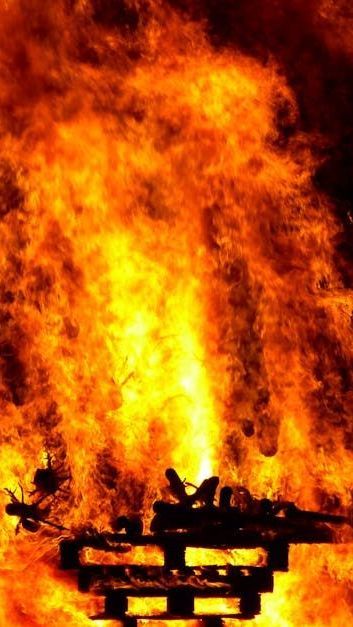 A large fire is coming out of a wooden structure.