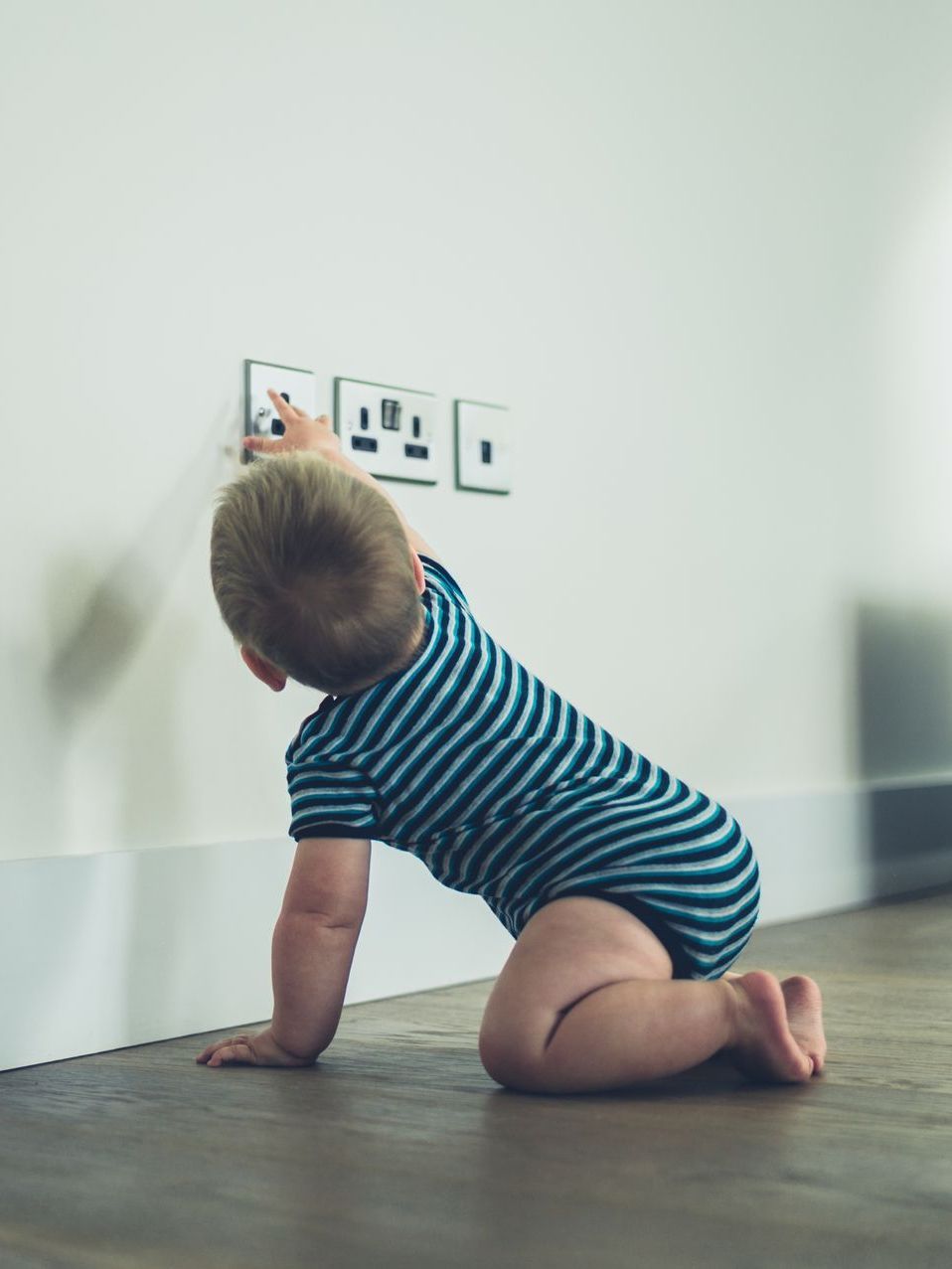 A baby in a striped shirt is crawling on the floor