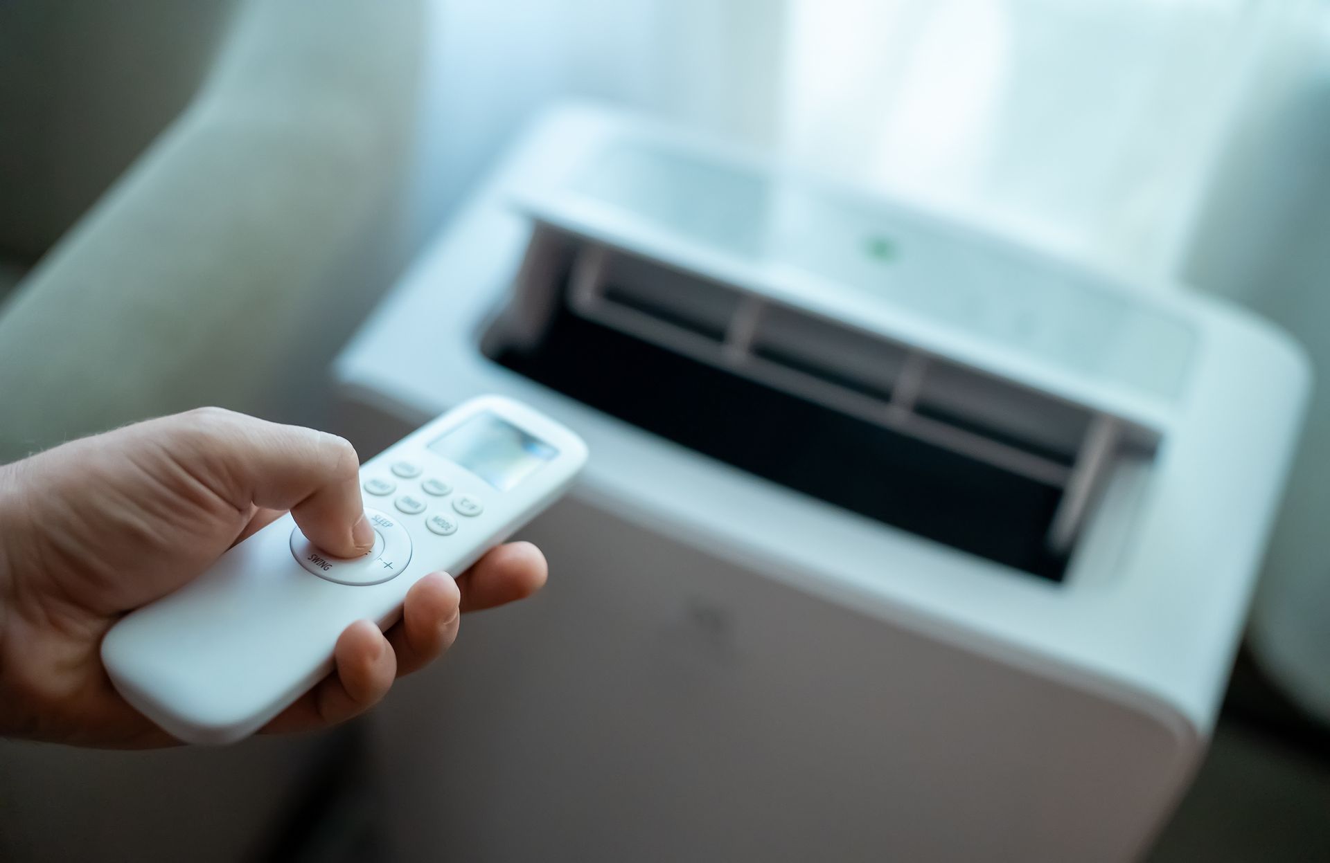 A person is holding a remote control in front of an air conditioner.