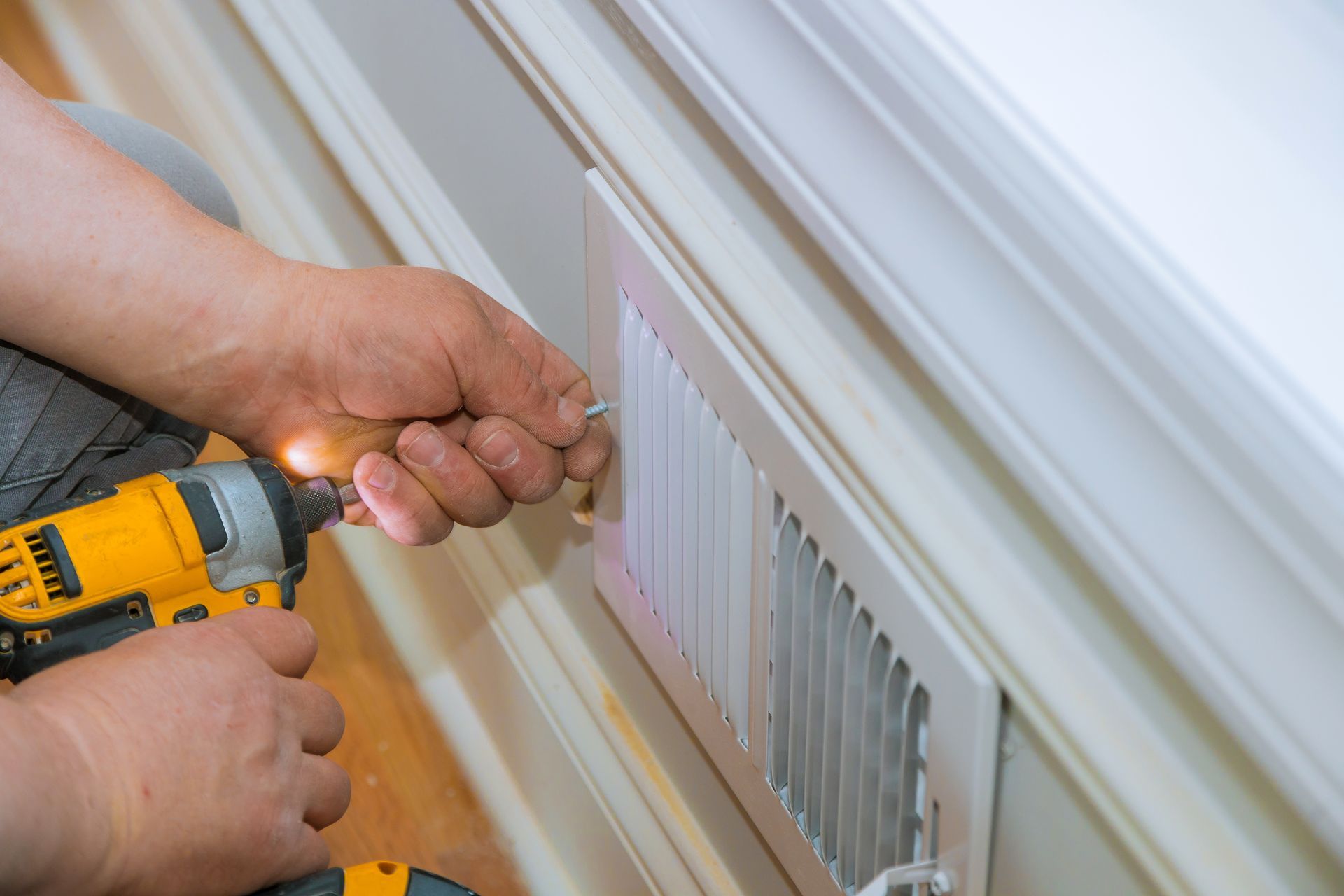 An electrician is using a drill to install a vent on a wall.