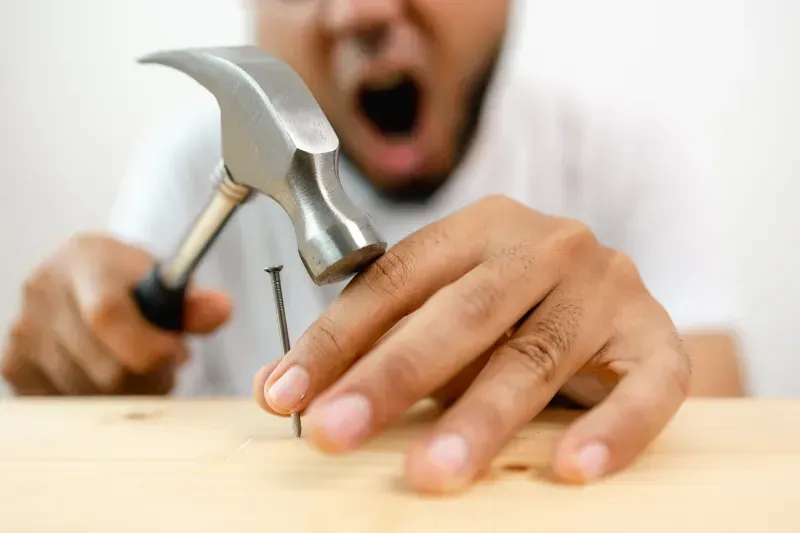 A man is hammering a nail into a wooden table.