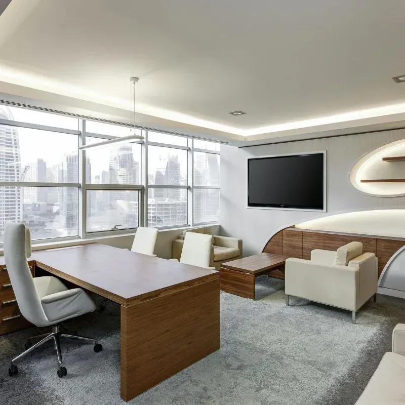 A modern office with a large table , chairs , and a flat screen tv.