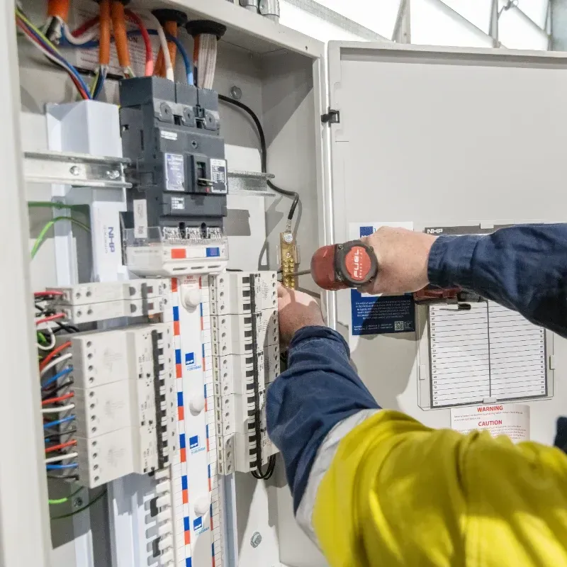 An electrician is working on an electrical box with a screwdriver.