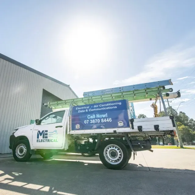An electrician work ute is parked in front of a building