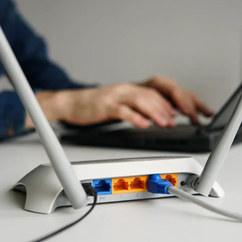 A person is typing on a laptop next to a router.