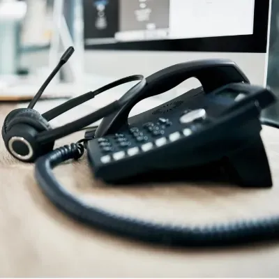 A telephone and a headset are on a desk in front of a computer.