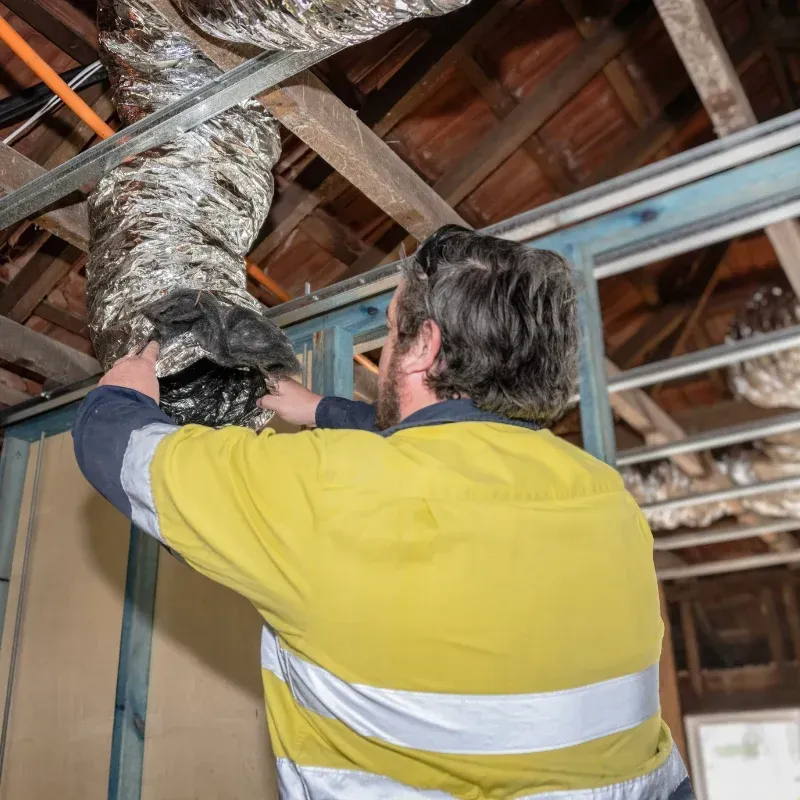 An electrician is working on an air duct in the ceiling of a building.