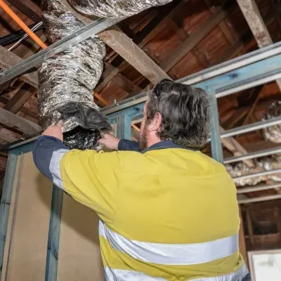 An electrician is working on an air duct in the ceiling of a building.
