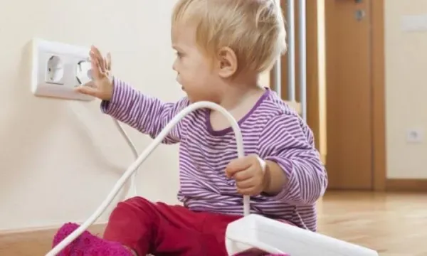 A baby is sitting on the floor playing with an electrical cord.