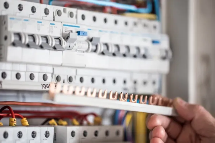 An electrician is holding a wire in front of an electrical box.