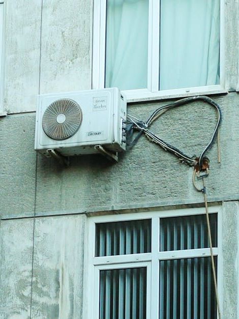 An air conditioner mounted on the side of a building next to a window