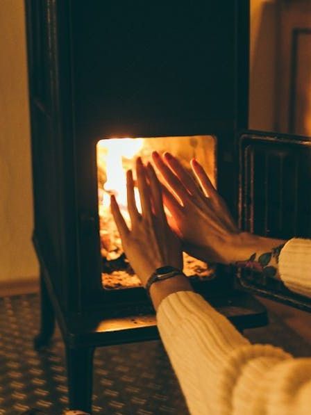 A person is warming their hands in front of a fireplace.