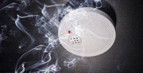 A smoke detector is surrounded by smoke on a black background.