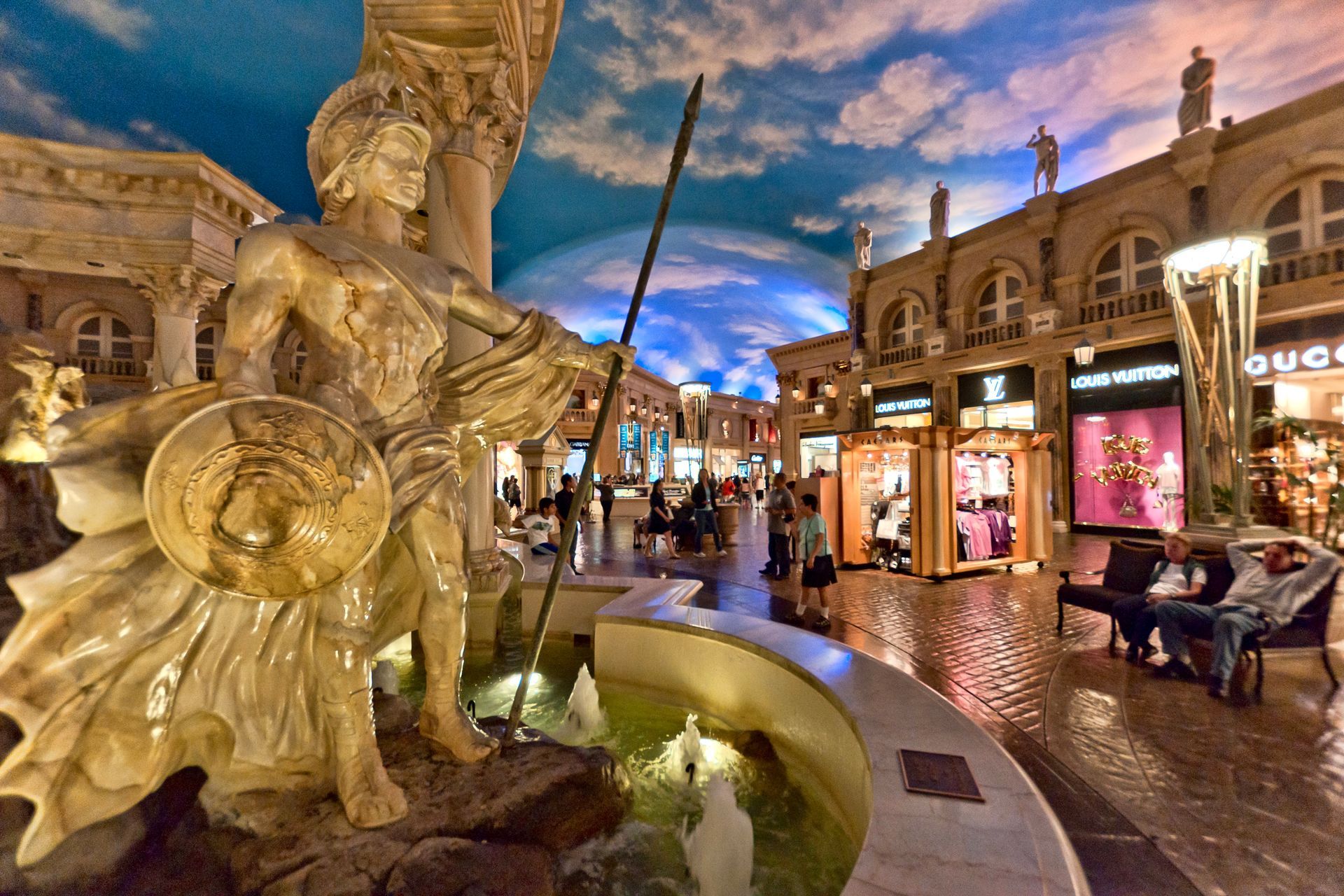 Roman-inspired statues and architecture beneath a painted blue sky inside The Forum Shops at Caesars Palace in Las Vegas.