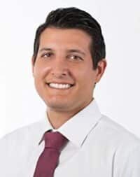 A man wearing glasses and a suit smiles for the camera