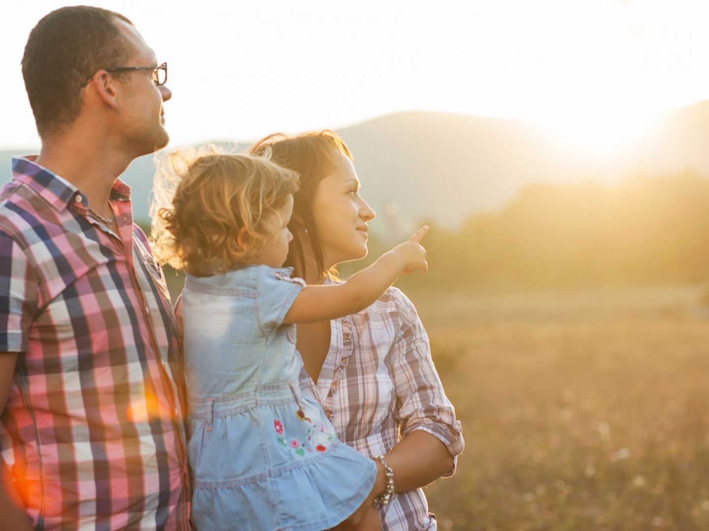 A family is standing in a field looking at the sun.