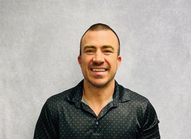 A man in a brown sweater is smiling for the camera.