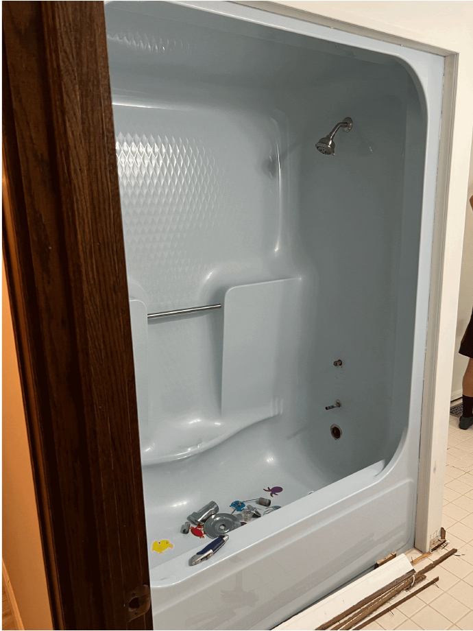 Empty, light-blue, accessible shower stall with seat, faucet, and showerhead. Brown door frame on left, white wall on right.