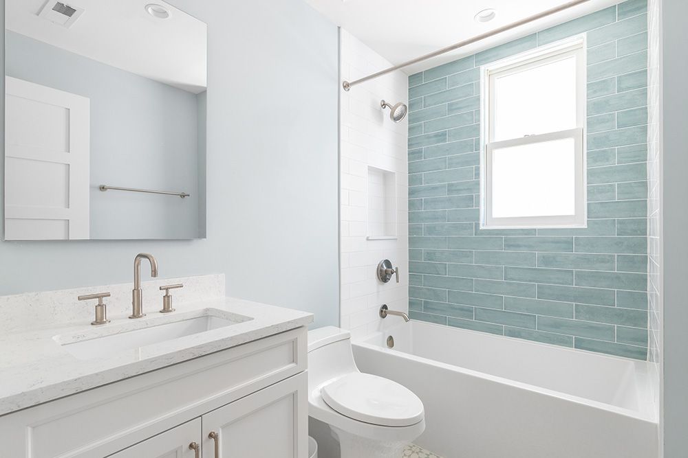 Modern bathroom with blue-tiled shower, white fixtures, and light blue walls.