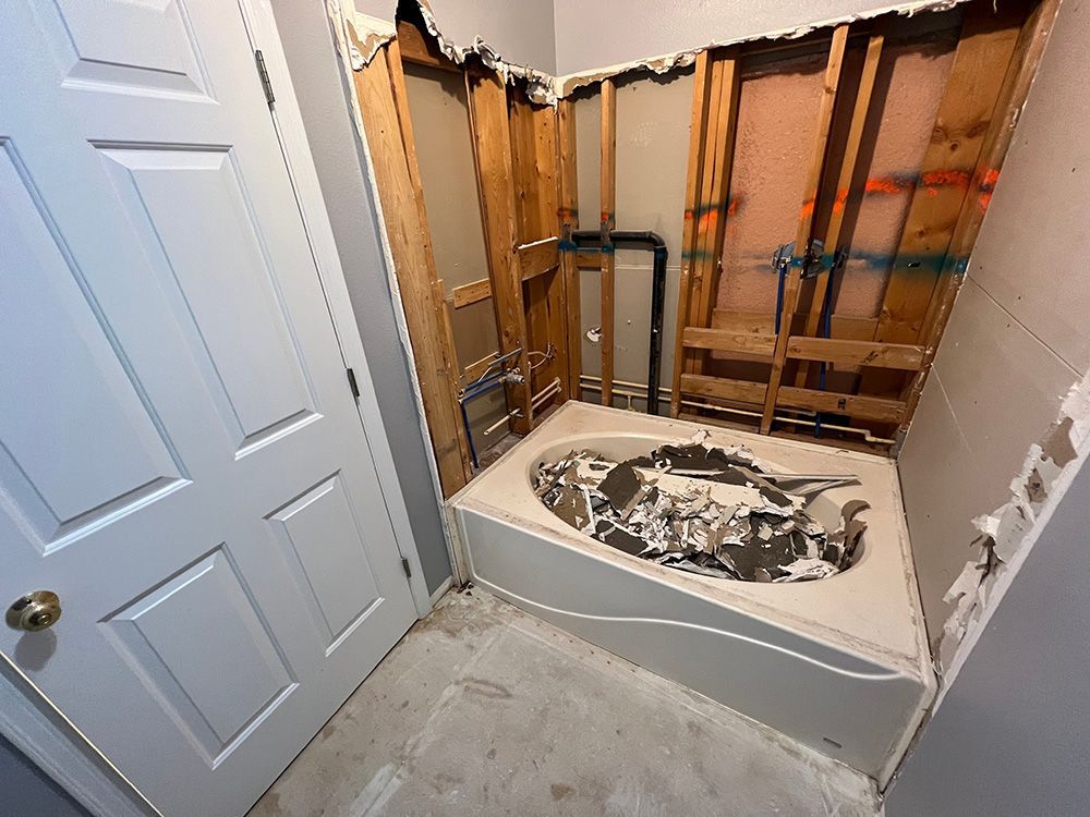 Bathroom remodel with exposed framing and tub; demolition debris in tub.