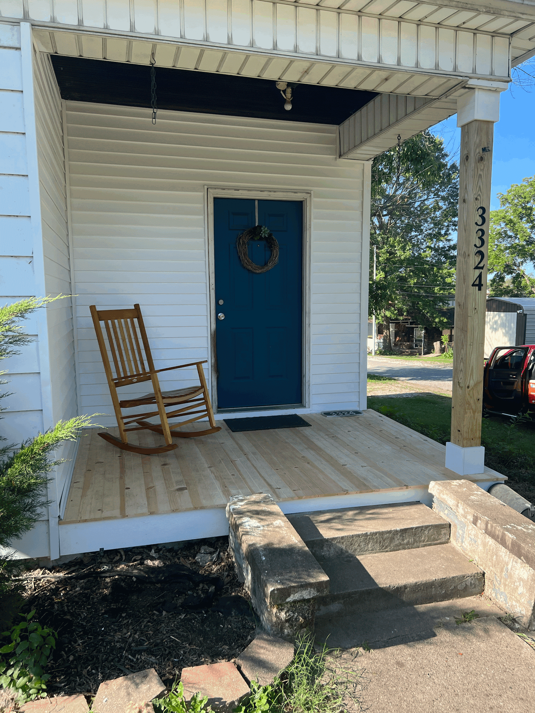 A white house with a teal door, porch, rocking chair, and address numbers.