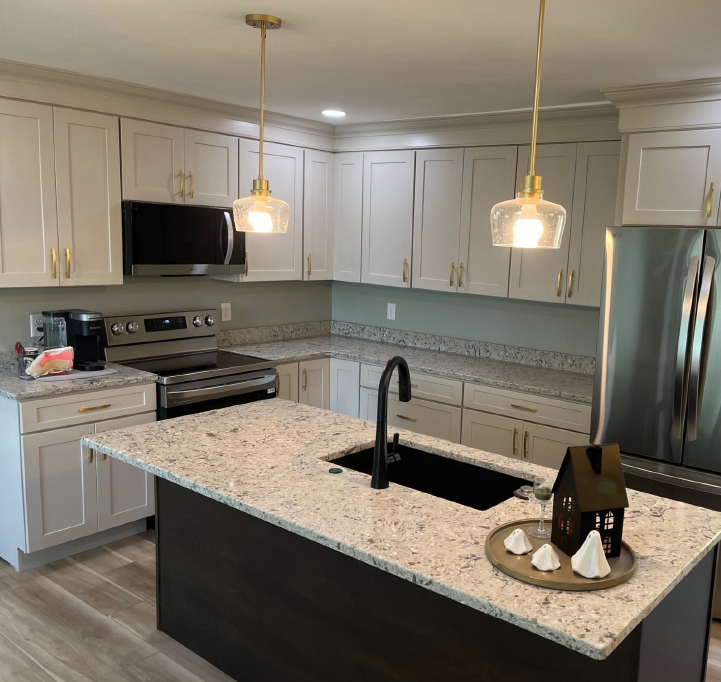 Modern kitchen with light gray cabinets, granite countertops, dark island, and brass pendant lights.