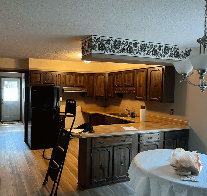 Kitchen with dark wood cabinets, black refrigerator, and light wood-look flooring.