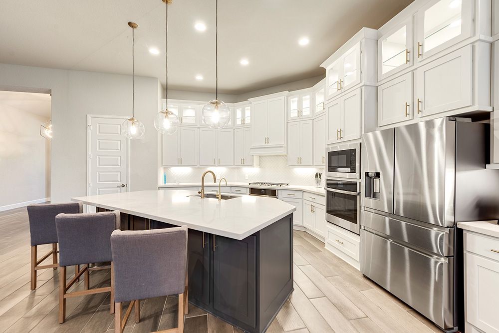 Modern kitchen with white cabinets, stainless steel appliances, a dark island, and pendant lights.