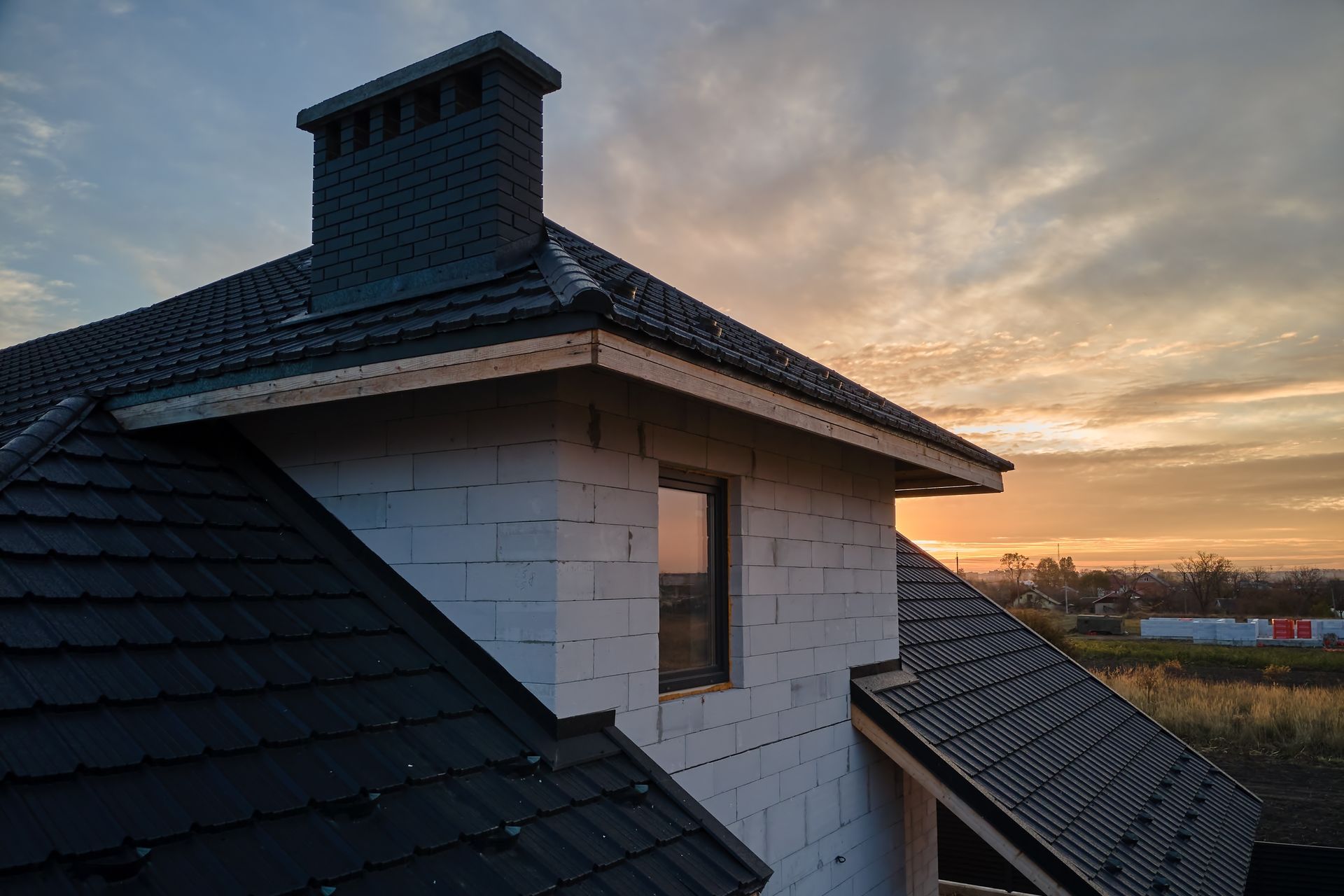 A house with a black roof, white brick walls, and a chimney against a sunset.