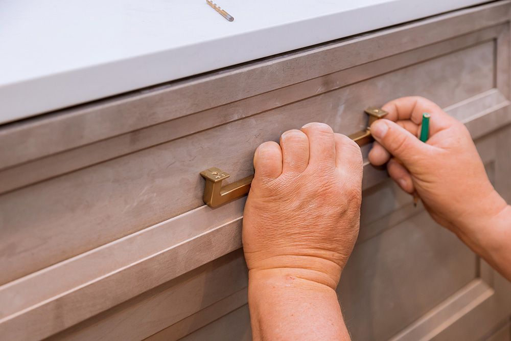 Person installing a brass drawer pull on a gray cabinet.